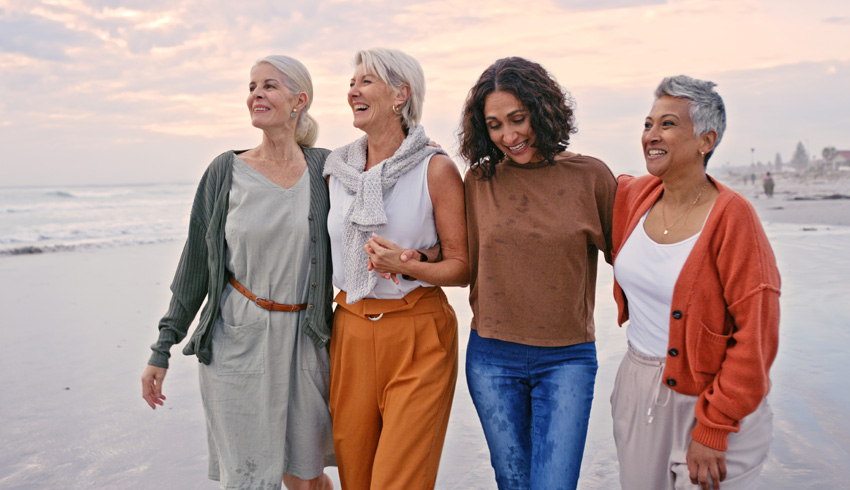 Four mature women walking together on the beach